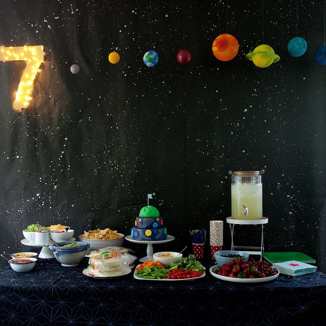 Outer space party table with night sky and planet backdrop and a delicious array of Space theme party food.