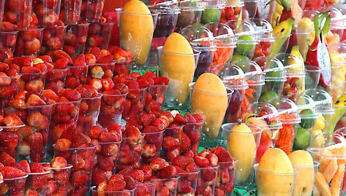 Fruits in the Chatuchak Street Market in Bangkok. Next to the strawberries are yellow peeled mangos and mixed fruits in plastic containers