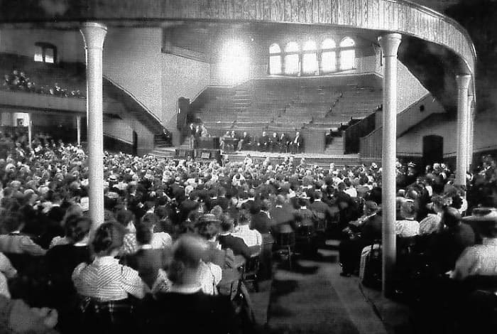 “Built in 1894, the auditorium on the Northfield campus seated 2,500 and was primarily constructed to serve the throngs of people attending Dwight L. Moody's summer conferences. In this photo, Moody is on stage, seated fourth from the right. Courtes