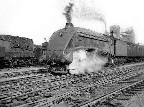 Class A4 Pacific No.17 'Silver Fox' on passenger duty passes rakes of tarpaulined wagons that could well have contained war materials made in the plant seen behind the express train