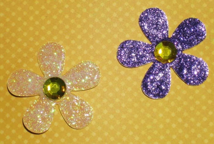 It is easy to create your own glitter glue flowers, Cut out a flower of your choice on heavy card stock. Paint the glitter glue on top of the flower petals, Allow to dry. Add a half gem to the top. Perfect for a scrapbook page or a card.