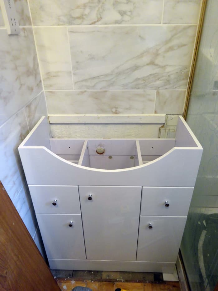 Installing the new vanity unit 5 inches forward of the back wall to allow water and waste pipes to be behind the cupboard, rather than inside.
