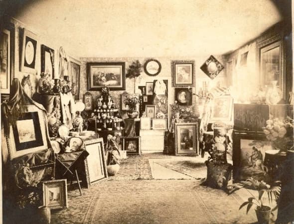 A period photo of a Victorian interior. Note the numerous framed pictures on the wall and the decorative objects on every available surface. Scroll down to see more room settings in our gallery of Victorian interiors.