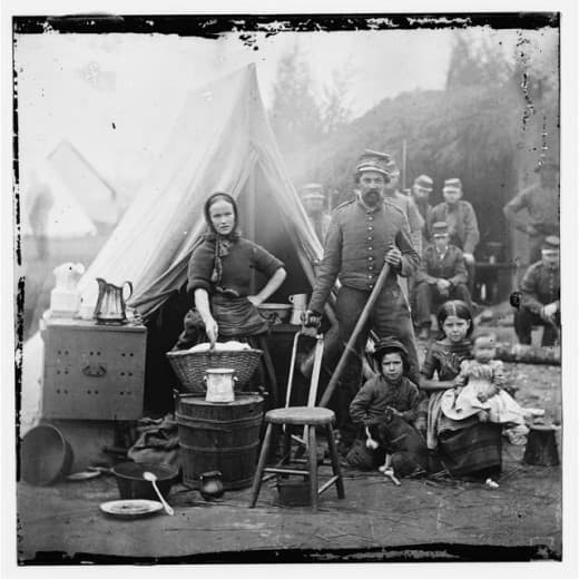 A wife and three children join a soldier in his camp. The wife holds a basket of laundry, so this was no holiday outing for her