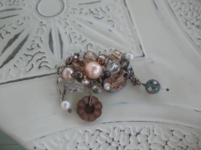 This wire-wrapped pin features freshwater pearls, glass beads, crystal and vintage buttons. Use chain to add dangles.