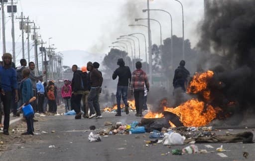 People walk past burning barricades during a protest against deficiencies in government services in Gugulethu, an impoverished township near Cape Town, in August 2012. - Protest in South Africa is on the rise and could lead to a fully-fledged revolt,