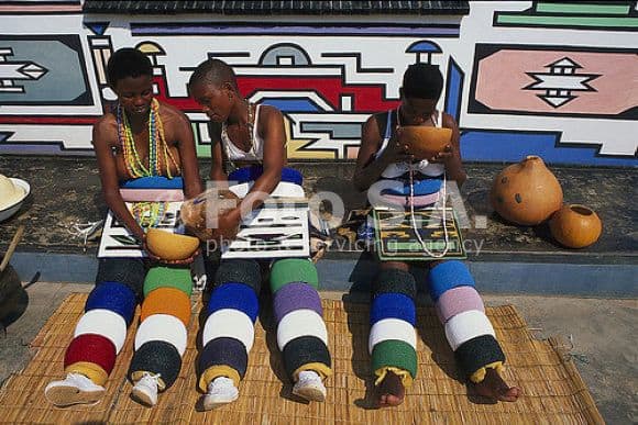 Ndebele girls in their traditional clothing and sitting next to their house they decorated themselves