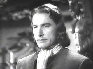 Errol Flynn's squarish face is made to look more even more square by the wavy, geometrical hairstyle that ends in both vertical and horizontal line with his chin.