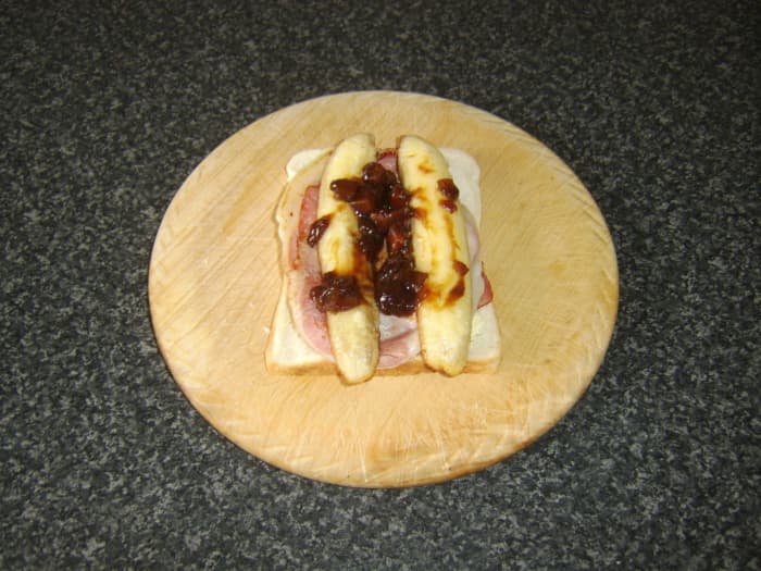 Two slices of middle bacon, a fried banana and a spoonful of chunky pickle ready to be topped with a second slice of bread