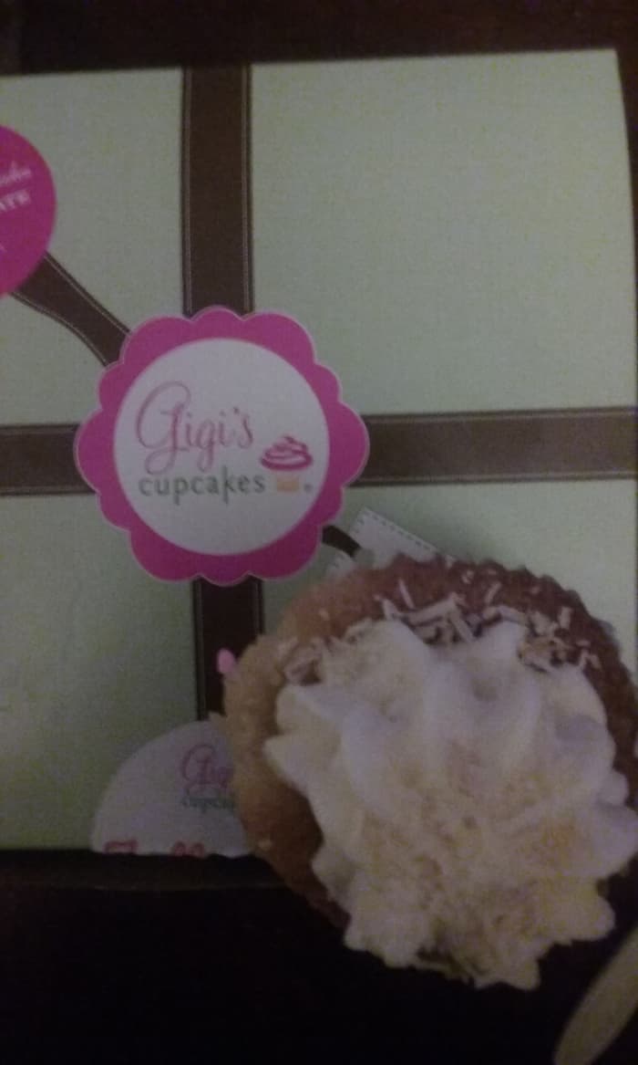 A delicious cupcake in the Italian wedding cake cupcake flavor sits atop the pretty signature green, brown and pink designed box from Gigi's Cupcakes