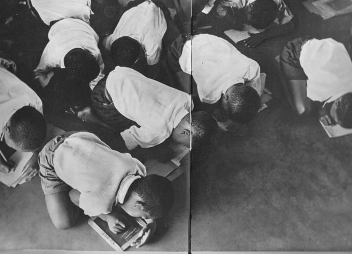 Students kneel on the floor to write. Government is casual and unwilling to furnish schools for Africans.