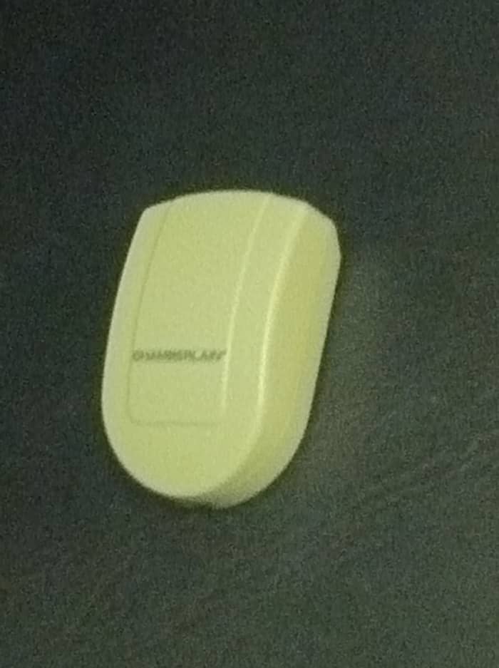 The sensor component attaches directly onto the garage door, signaling the receiver indoors whether the door is open (red light) or closed (green light).