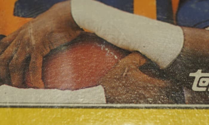 This is a 1987 Topps Box Bottoms of Eric Dickerson. It's graded PSA 3. Although you couldn't tell that by looking at it from afar, one major problem is surface damage. The football has a visible scratch.