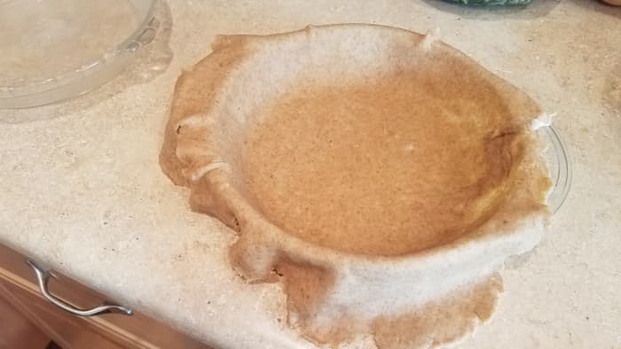 And transfer your dough over. I do this by gently folding it twice to get it off of the counter without tearing, and then unfolding it in the pie dish.