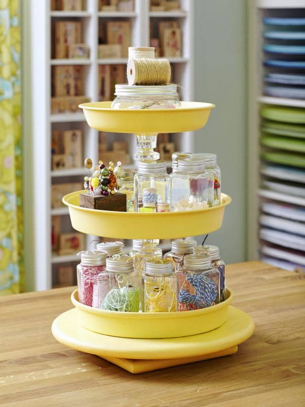 Use a lazy susan and some cake pans to create your own tired storage unit, Spray paint and glue the pans.Inexpensive glass candle holders are used in between the layers, Many of these can be found at your local dollar store or thrift shops.