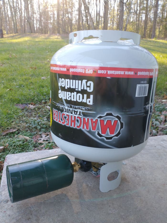 Propane bottle attached to refill adapter on a larger propane tank, ready to be refilled.