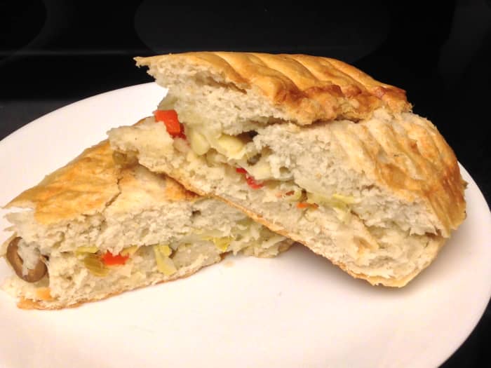 Muffaletta panini with olives, pickled vegetables, provolone, and artichoke hearts on baguette.