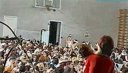 A view inside the gym, people packed in shoulder to shoulder, bombs visible strung between the basketball hoops