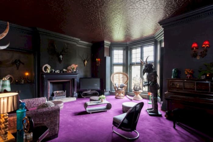 The Scorpio living room: a purple-blue carpet, rounded furniture, items in black and gray, gothic elements, and an inviting fireplace.