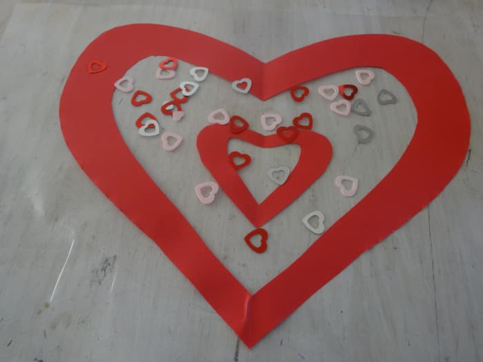 Lay the piece of contact paper on the surface sticky side up and lay the heart shape and a smaller heart and/or any other decorations on it.