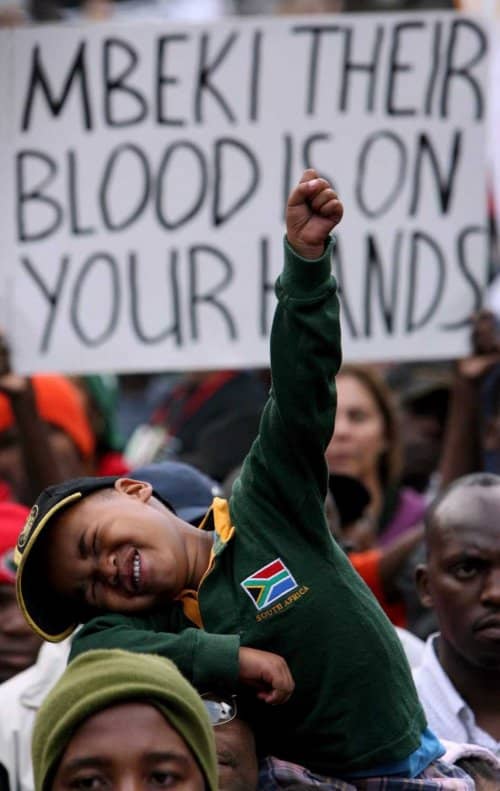 President Mbeki under placard and protestors attack for dragging the country under and exacerbating the AIDS pandemic. A Kid Encapsulates the fighting spirit of the African people in this picture