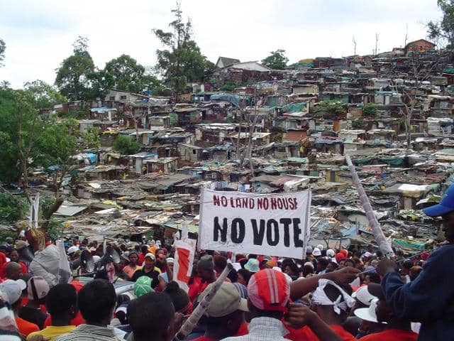 Abahlali baseMjondolo, holding a rally, and the shack dwellers ramshackle houses in the background, and they were holding a sign that read: "No Land! No Houses! No Vote
