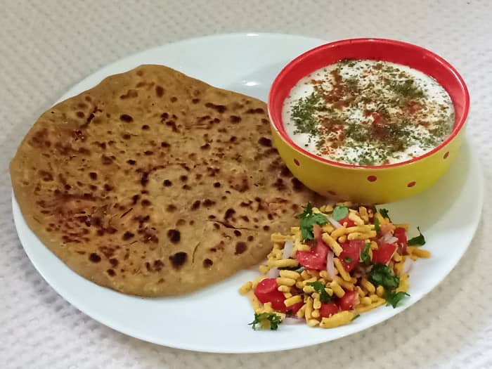 Sev paratha is crisp, spicy, and tangy. Served here with yoghurt sprinkled with some mint powder, roasted ground cumin seeds, red chilli powder, black pepper powder and the sev mixture made with sev, chopped onion, tomato, and cilantro.