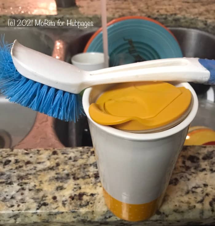 A dish brush and a ceramic cup containing bleach, dish soap, and water provide a quick way to clean dishes throughout the day.