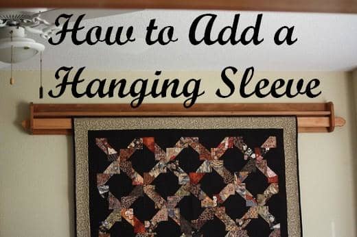 With this quilt holder, a piece of wood is inserted in the hanging sleeve and placed on the hanger that is attached to the wall.