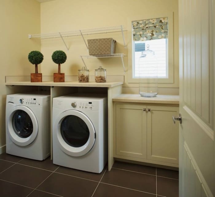 Lovely pale yellow laundry room with cream cabinetry with white laminate countertops and the white front-load washer and dryer.