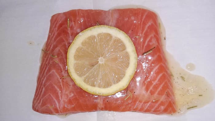 Glaze each salmon fillet with lemon butter sauce and then place a lemon slice on top. Now it's ready to bake.