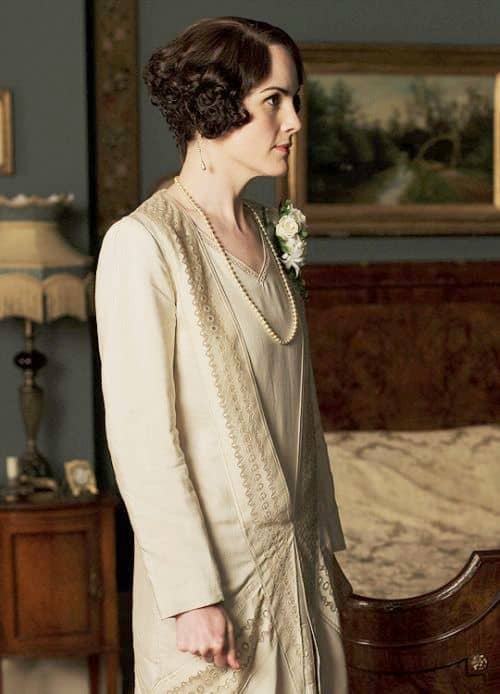 She skips the white dress for a demure ivory suit with a dropped waist, accessorized with a simple strand of pearls, and a corsage of white flowers.