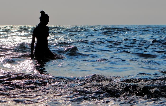 A woman wades in the ocean's vast water as she contemplates.