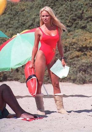 Bay Watch blond babe in red swim suite sporting Uggs and surfboard and life saving tube on the beach