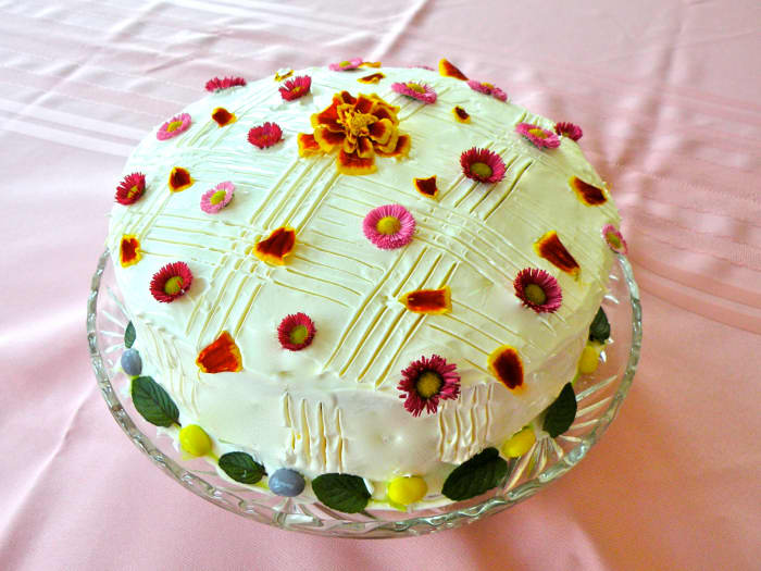 English Daisies are strewn over cake top along with petals from a marigold. A full marigold is used in the center.