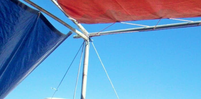 This overhead tarp has running rigging to keep it from being torn apart by the wind. The entire frame has guylines going out at an angle to rebar stakes to keep it affixed to the ground. Notice the side, shade tarp hanging at an angle from zipties.