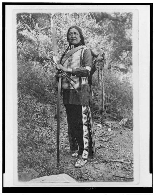 Chief Standing Bear (possibly Luther Standing Bear) full-length portrait, standing, facing slightly left, holding bow and arrows.