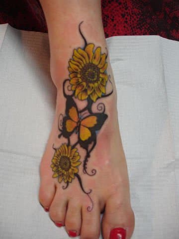 This tattoo covers most of the wearer's foot with a butterfly fluttering between two sunflowers.