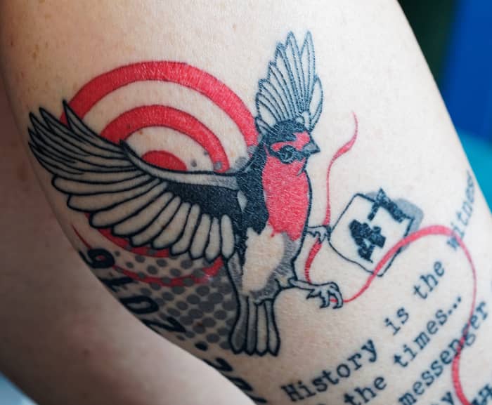 Tatuaggio di un uccello che incorpora testo e altri simboli.