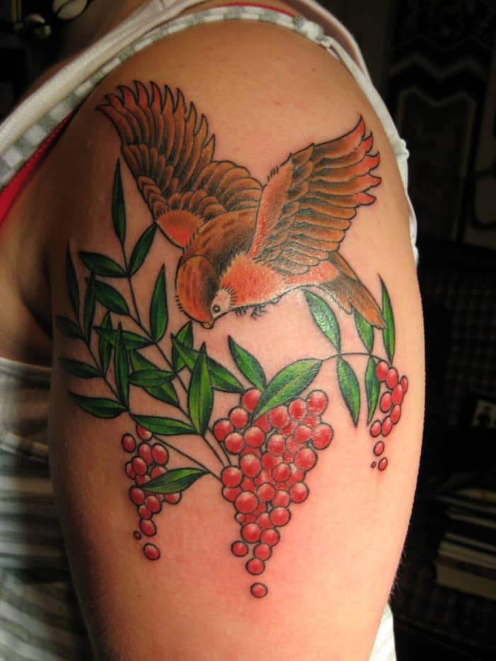 Ein lebhaftes Tattoo eines Vogels, der über roten Beeren schwebt.