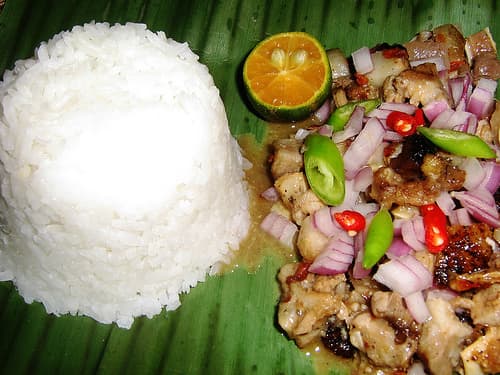 Spicy pork sisig with chili and calamansi served with steamed rice on a banana leaf