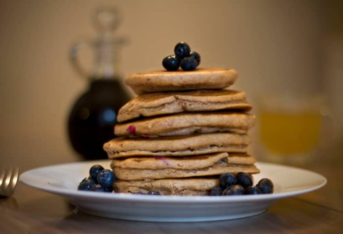 A fresh stack of cinnamon blueberry pancakes ready to eat, with syrup and apple juice