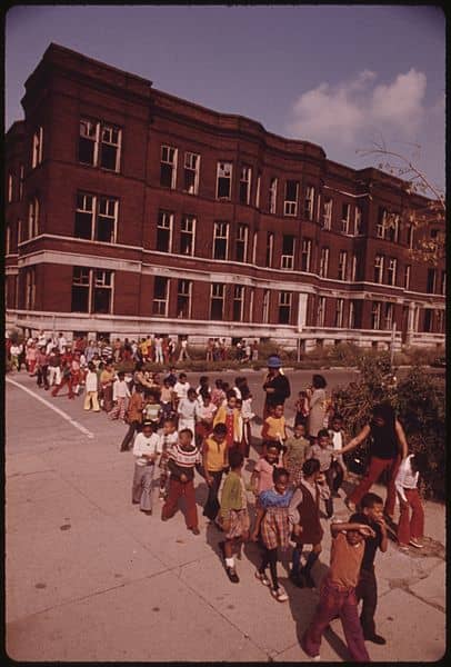 YOUNGSTERS RETURNING TO CLASS FOLLOWING A FIRE DRILL IN A CHICAGO ELEMENTARY SCHOOL. FIRE DRILLS ASSUME A GREATER IMPORTANCE IN THE GHETTO SCHOOLS WHERE AREA BUILDINGS ARE MORE VULNERABLE TO VANDALISM AND FIRE. NOTE THE VACANT BUILDING WITH BROKEN WI