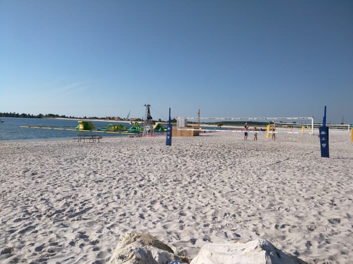 Wide shot of sandy Beachfront, Floating Inflatable Playground and Beach volleyball courts