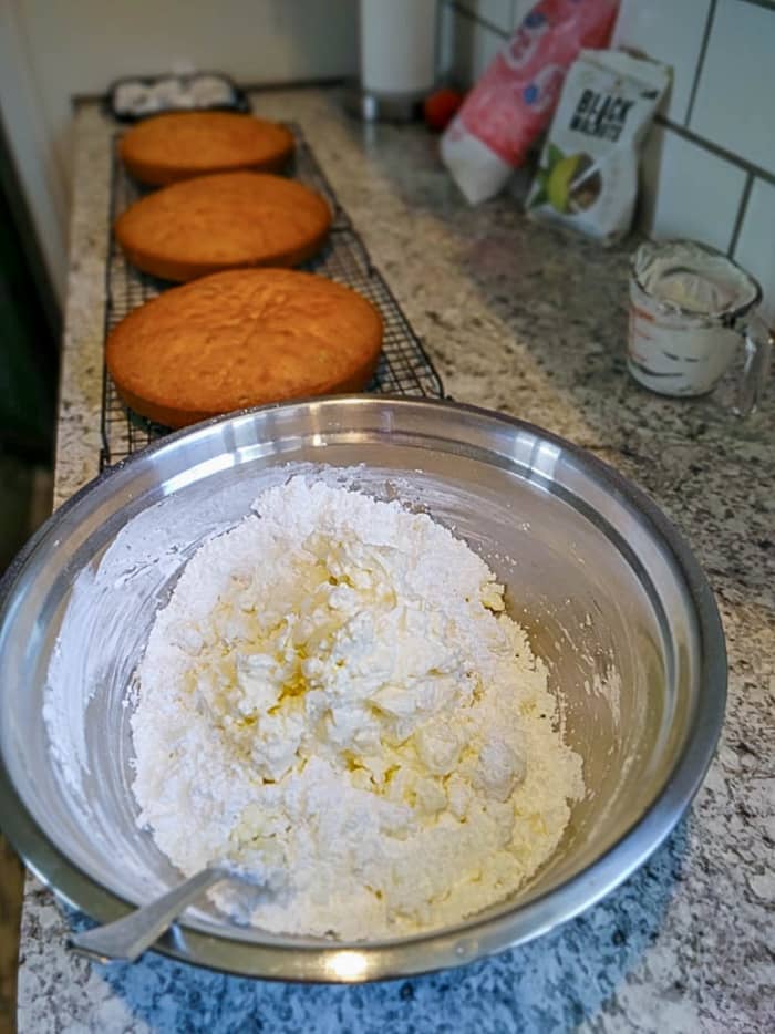 Three black walnut cakes cool while I make cream cheese icing in a bowl.