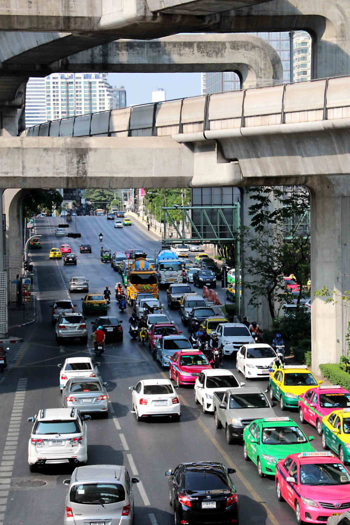 Traffic in Central Bangkok. Cars (note the brightly coloured taxis) and above them are the concrete walkways and supports of the BTS Skytrain service