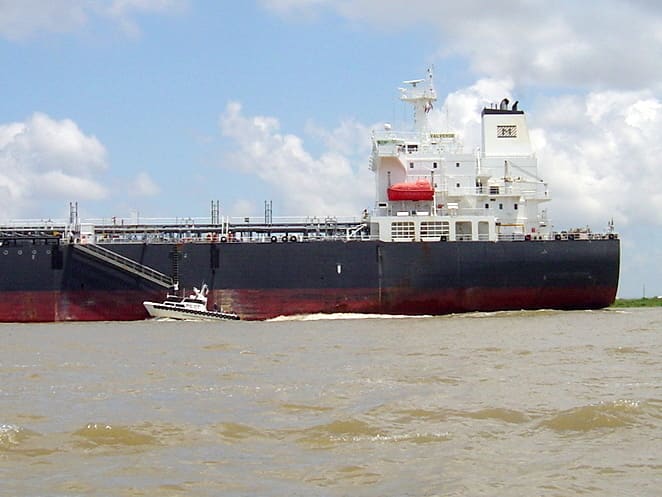 A pilot boat brings an experienced pilot for a tanker on the Mississippi River. At left, see the white-shirted pilot starting to climb up the sloping ladder, as both vessels travel at a fast speed.