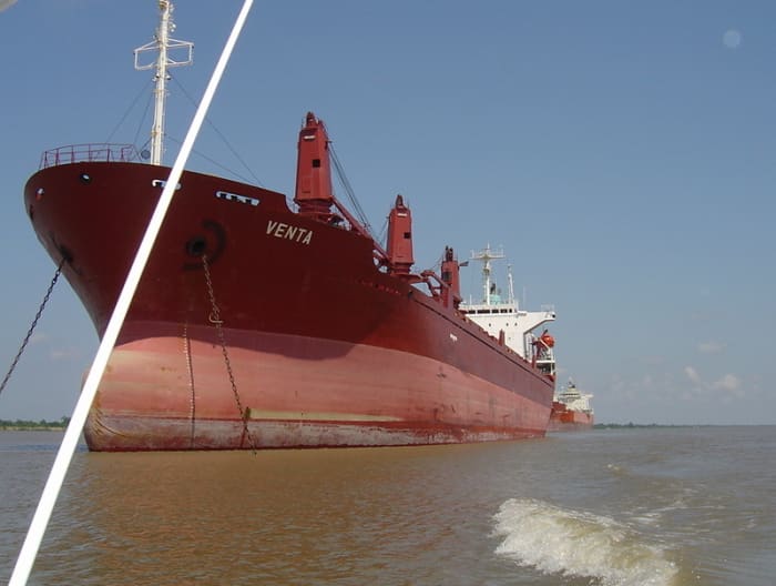 A large dry bulk hauler heads from the mouth of the Mississippi River northward toward New Orleans to pick up a load. The water line halfway up the hull is evidence that the ship is empty.