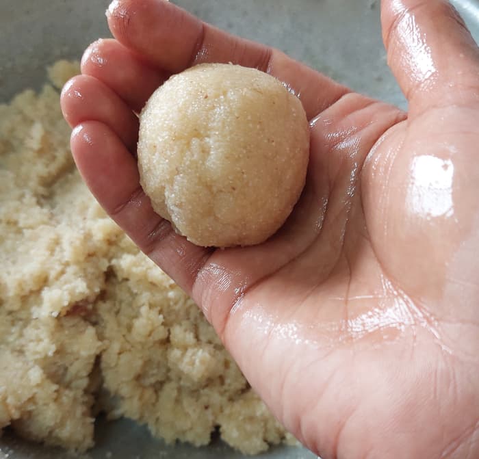 Let the mixture cool down slightly. Moisten your hand with some drops of ghee and shape ladoos (take small portion of the mixture to your palm, press well to bind it).