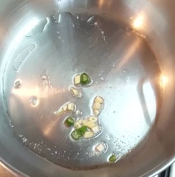In a pan, heat 2 tablespoons oil. Add 3-4 chopped garlic cloves and 1-2 chopped green chilies. Saute.